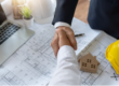 two men shaking hands over a blueprint