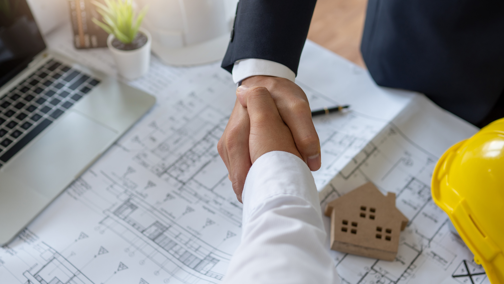 two men shaking hands over a blueprint