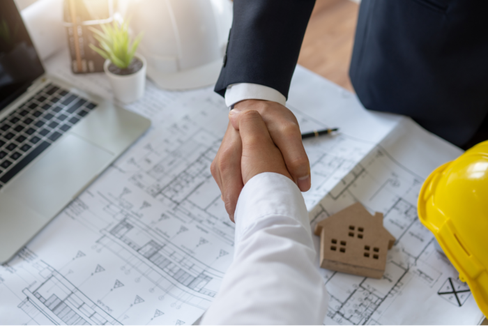 two men shaking hands over a blueprint