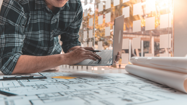 Man working on computer looking at blueprints Man working on computer looking at blueprints